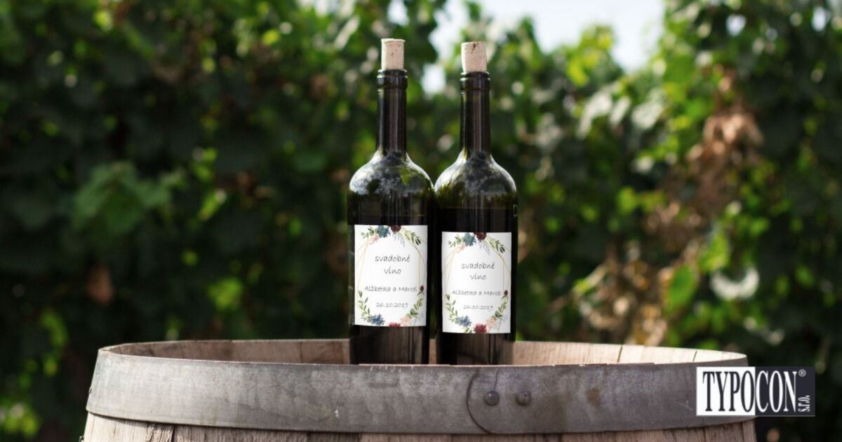 Dve vínne fľaše so samolepiacimi nálepkami na svadbu, ktoré sú položené na sude v záhrade. 